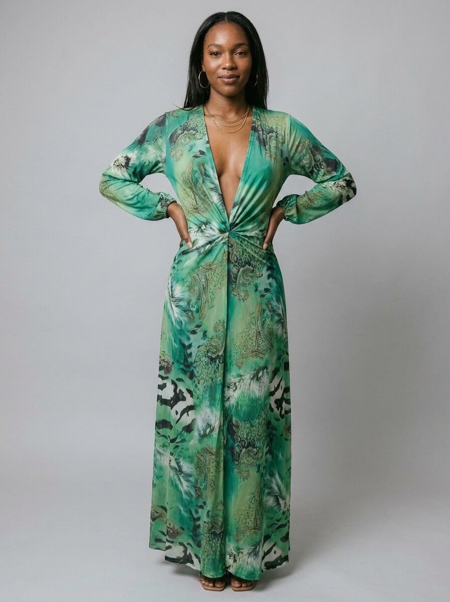 A woman modeling a long-sleeve green maxi dress with a deep V-neckline, front twist detail, and an abstract botanical print, set against a plain gray studio background.
